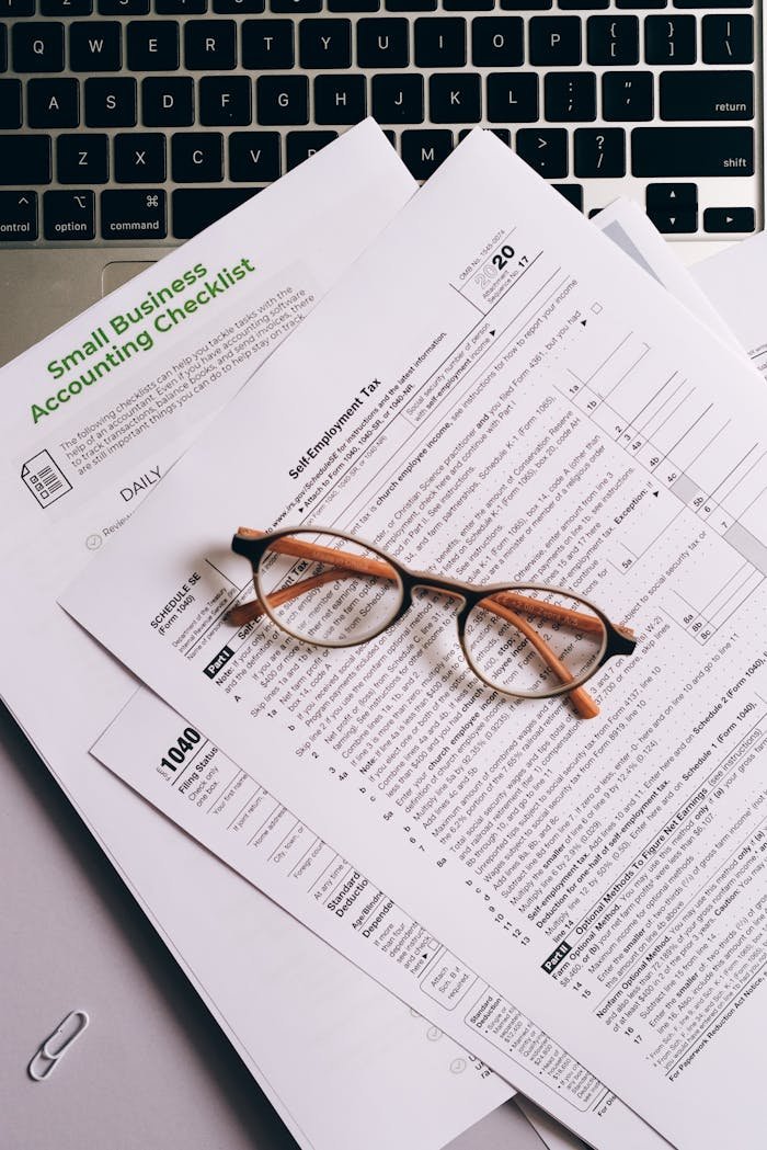 Overhead view of tax documents and eyeglasses on a laptop keyboard, ideal for finance or accounting themes.